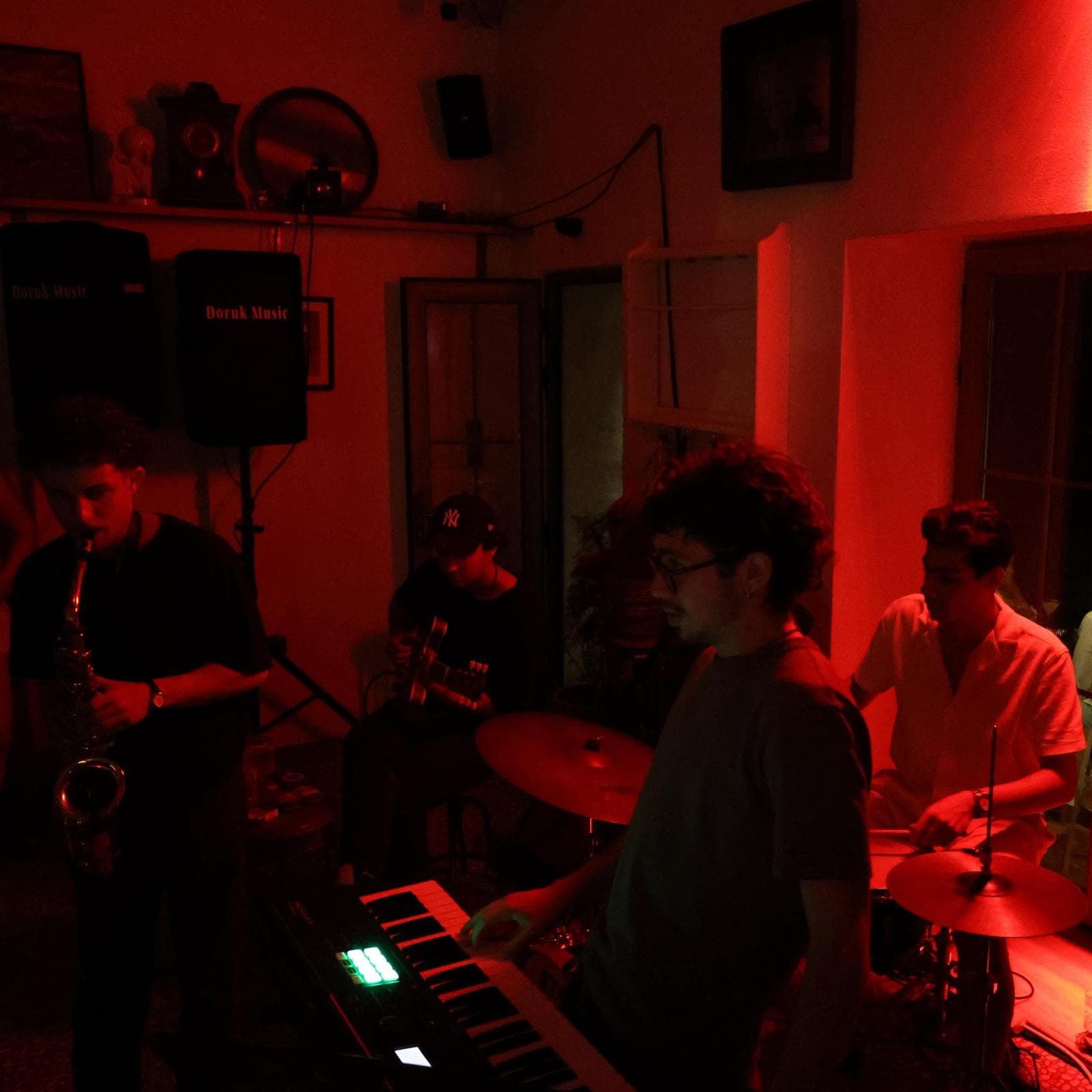 Maymun Collective playing an intimate show bathed in red light — sax, keys, guitar, and drums.