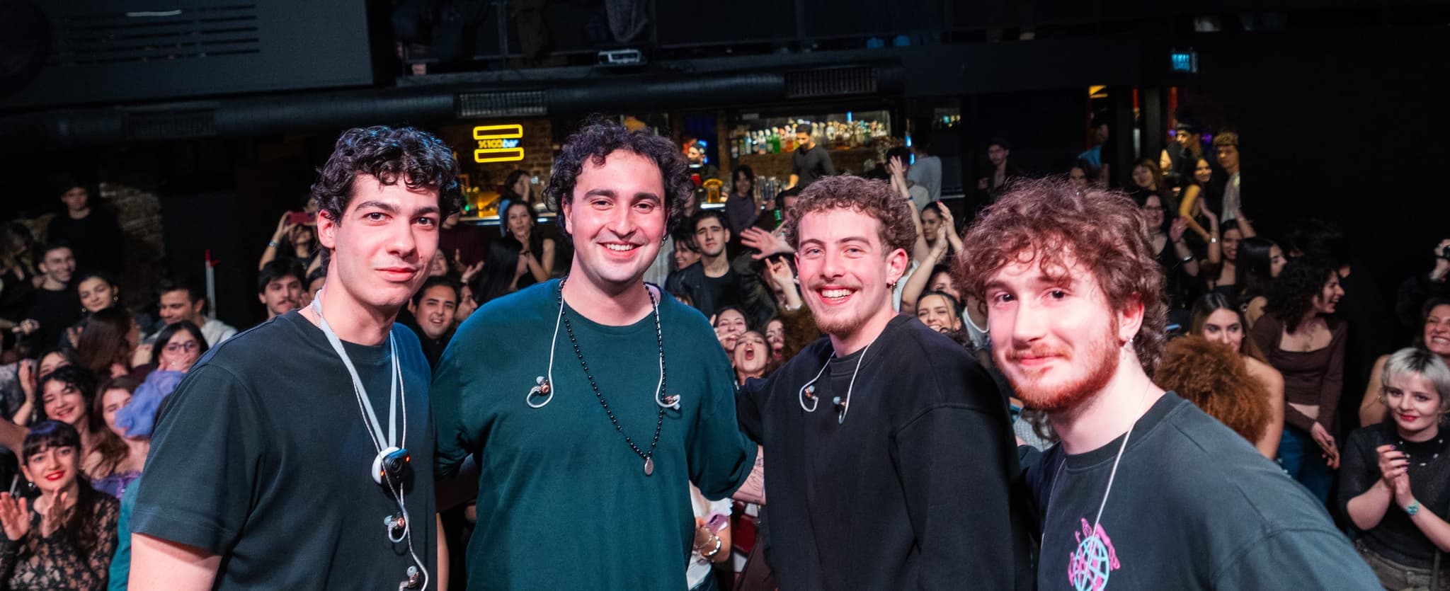 The four members of Maymun Collective posing together in front of a packed crowd after a show.