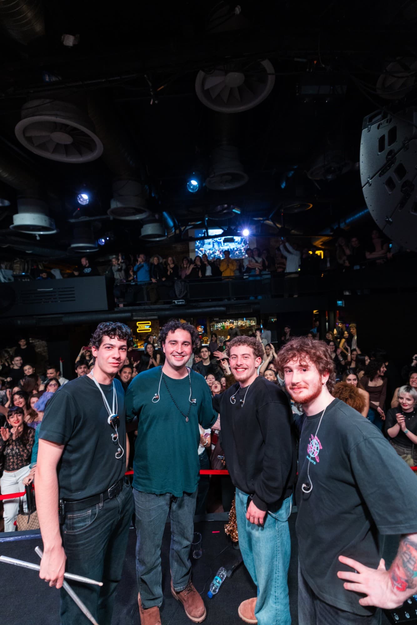 Four members of Maymun Collective on stage at a show, the crowd cheering behind them.